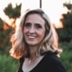 blonde woman with the glow of sunset behind her, 
             she's wearing a black shirt and a pretty smile